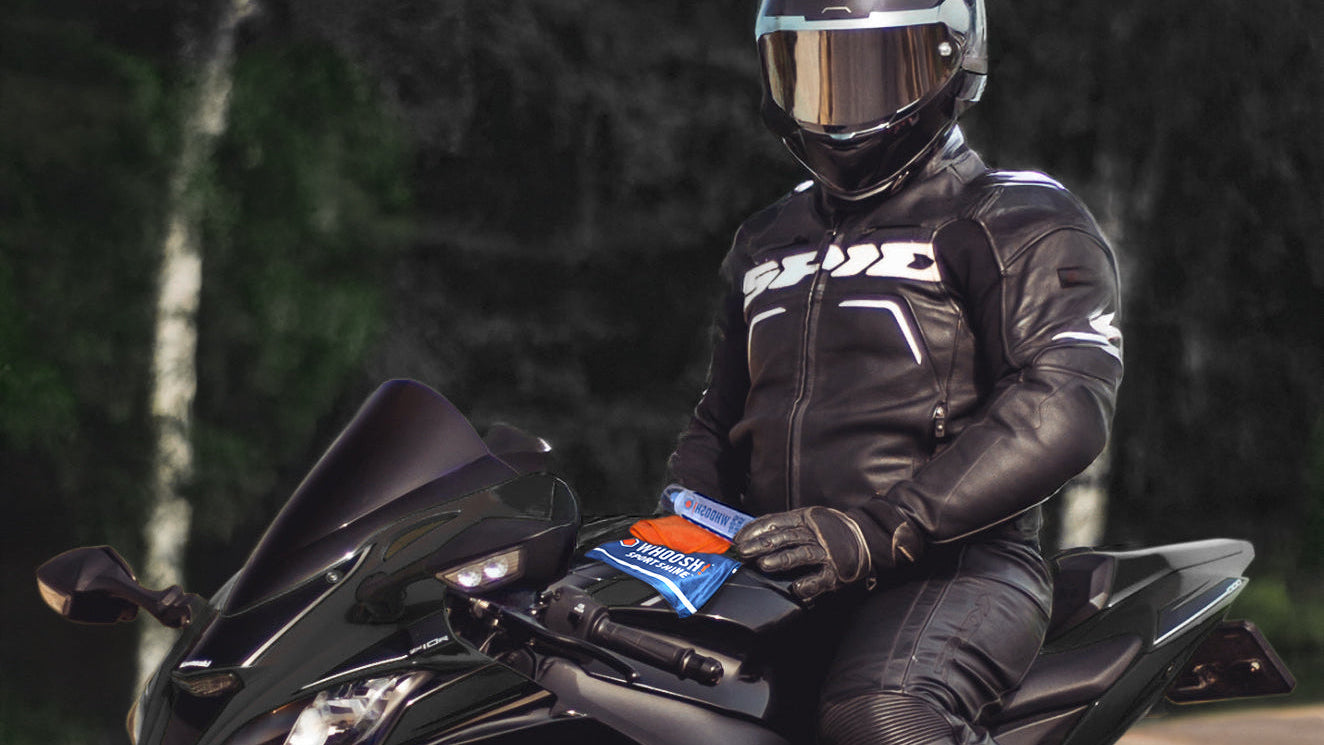 Person in black motorcycle gear sitting on a black motorcycle with a blurred forest background. WHOOSH! Sport Shine is laying in front of the rider.