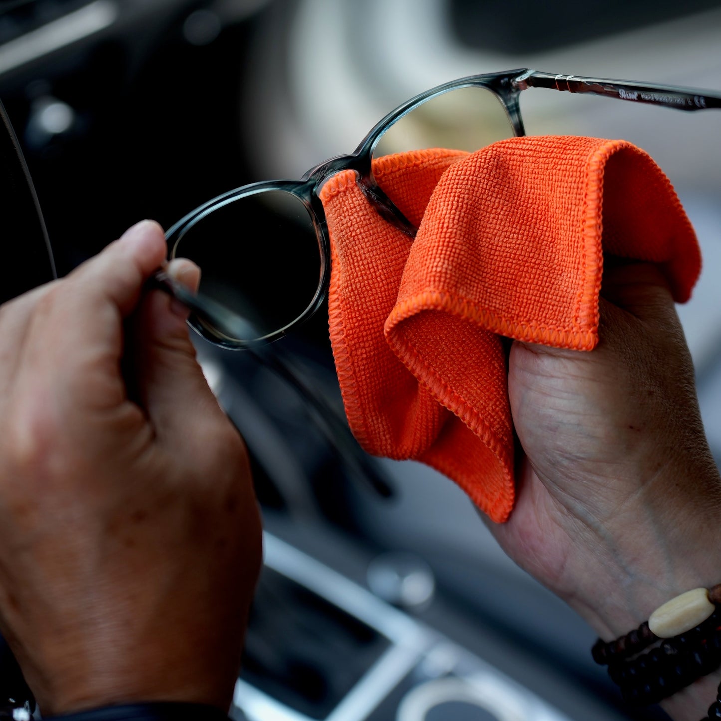 Person cleaning sunglasses with an orange cloth inside a car.